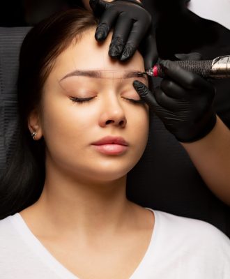 Beautician in gloves applying permanent brow makeup to an attractive brunette woman. Closeup shot