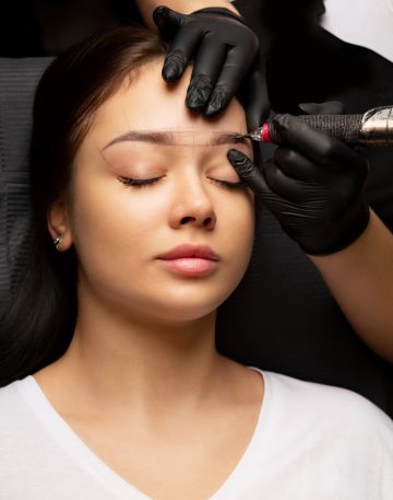 Beautician in gloves applying permanent brow makeup to an attractive brunette woman. Closeup shot